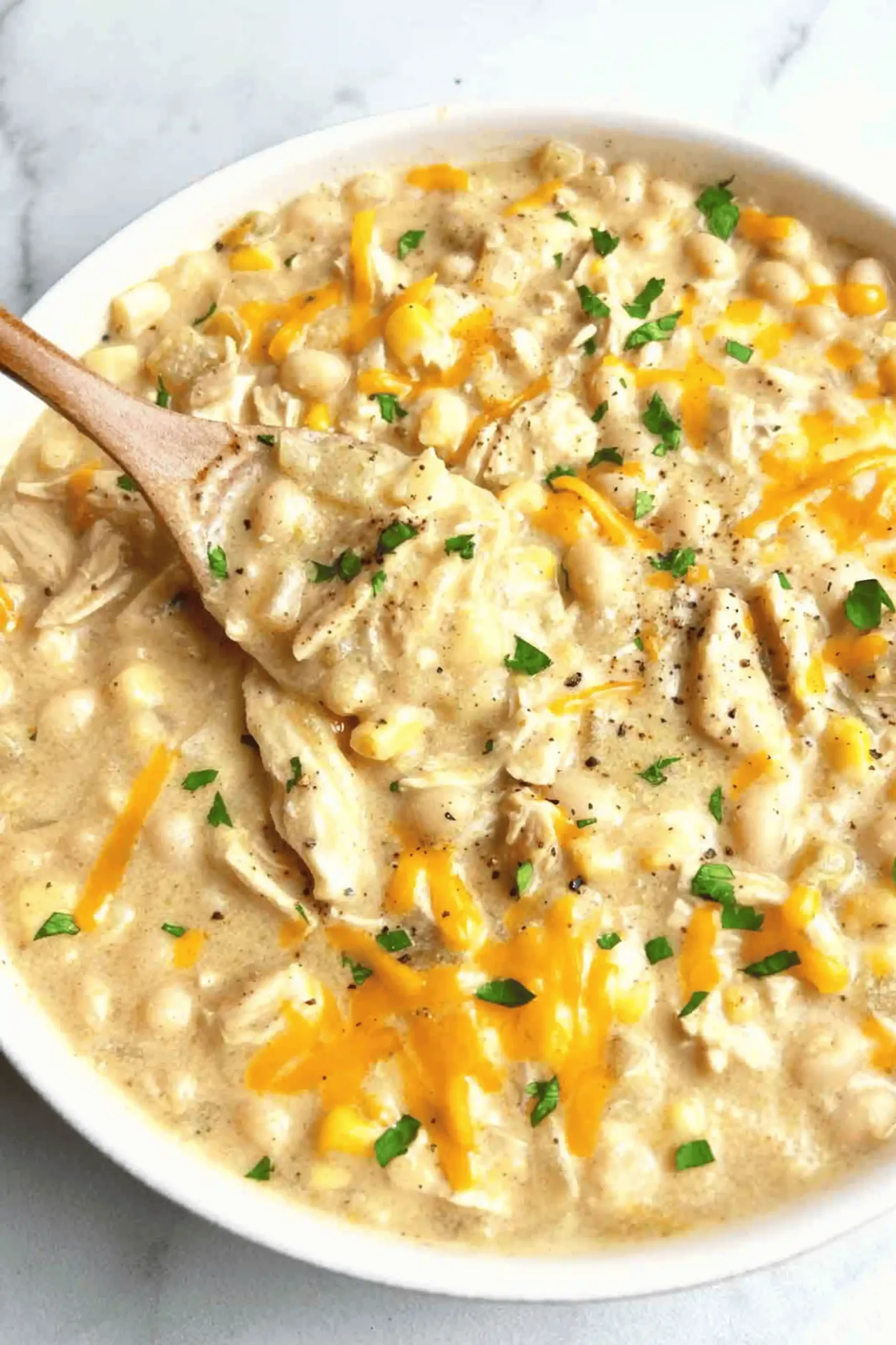 Top-down bowl of creamy white chicken chili with shredded chicken, white beans, green chiles, avocado, cilantro, Monterey Jack, tortilla strips, and a lime wedge on a light background