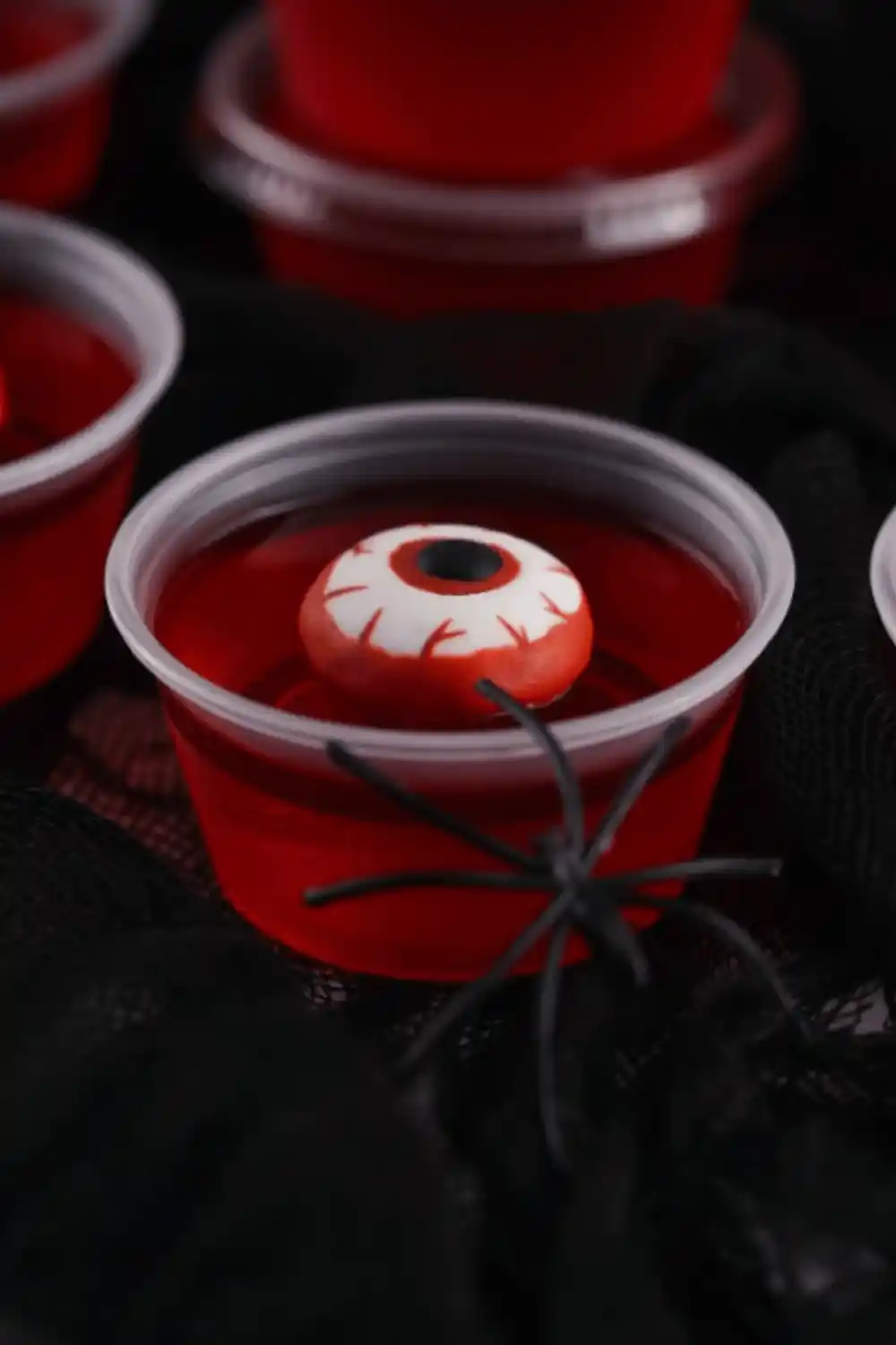 Spooky Halloween eyeball jello shots made with red strawberry gelatin and candy eyeballs, served in clear cups on a festive party table.