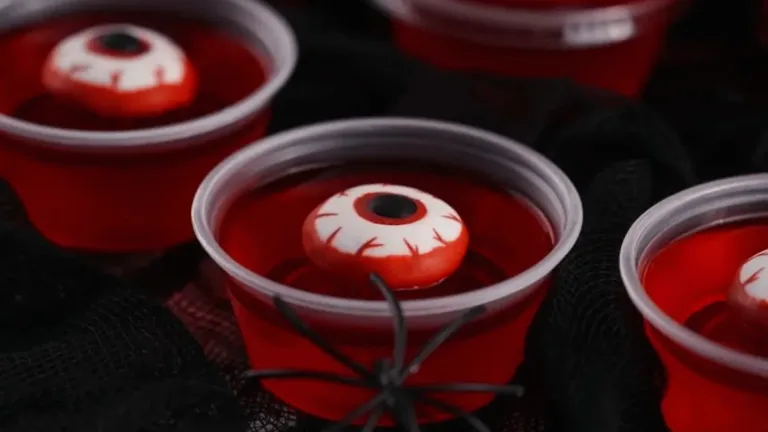 Red gelatin Halloween cups topped with candy eyeballs and a black plastic spider for spooky party treats.